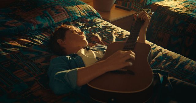 Medium shot of Kasey laying on a hotel bed playing guitar